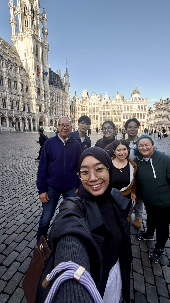 Six Student Consultants from Thunderbird School of Global Management stand with PTPI Director General Chalks Corriette on the Grand-Place in Brussels, with the Town Hall behind them, on the first day of their PTPI 2.0 project.